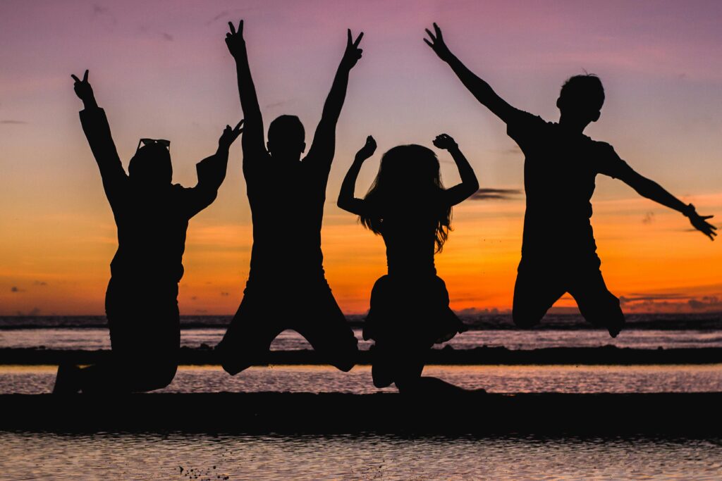 Silhouette of friends jumping on the beach at sunset, celebrating summer fun.